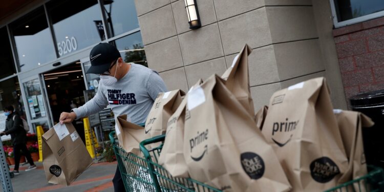 A delivery worker with a cart full of bagged groceries.