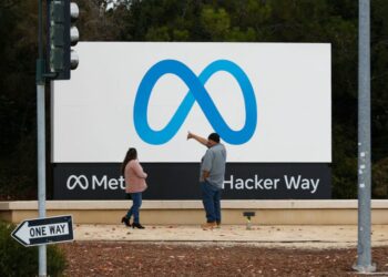 People stand in front of a Meta sign at the headquarters of Meta Platforms.