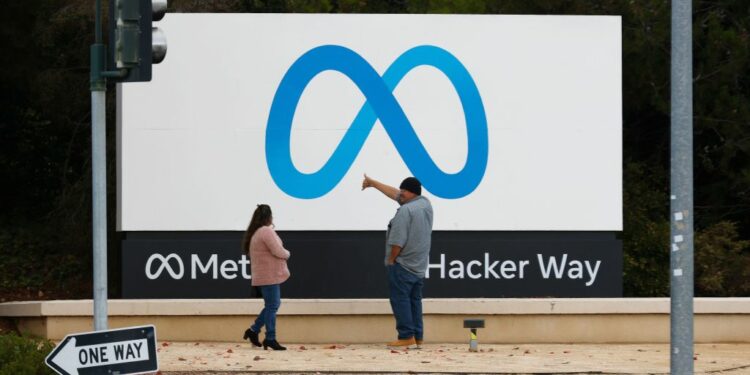 People stand in front of a Meta sign at the headquarters of Meta Platforms.