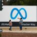 People stand in front of a Meta sign at the headquarters of Meta Platforms.