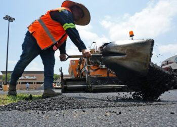 A worker shovels hot asphalt during a parking lot resurfacing job.