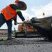 A worker shovels hot asphalt during a parking lot resurfacing job.