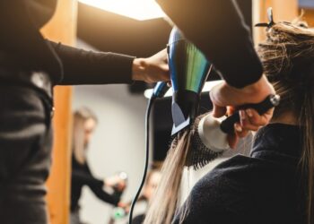 Master woman hairdresser dries the girl's hair with a hairdryer after washing in a beauty salon, close up.
