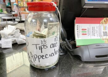 A clear jar filled with money and a label that appears to be made of paper sitting on a table in a restaurant in the Bronx, NY.