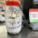 A clear jar filled with money and a label that appears to be made of paper sitting on a table in a restaurant in the Bronx, NY.