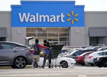 A man pushing a shopping cart in front of a Walmart store.