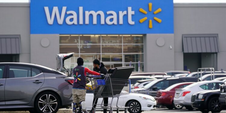 A man pushing a shopping cart in front of a Walmart store.