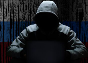 A hacker sitting with a hood against a backdrop of binary code.