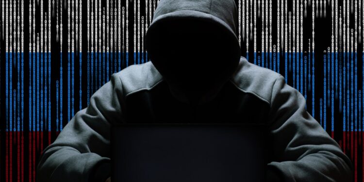 A hacker sitting with a hood against a backdrop of binary code.
