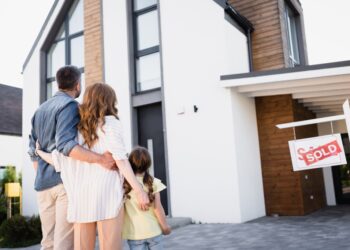 Back view of a family standing near a 'Sold' sign in front of a house