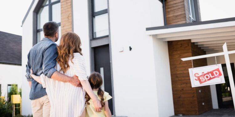 Back view of a family standing near a 'Sold' sign in front of a house