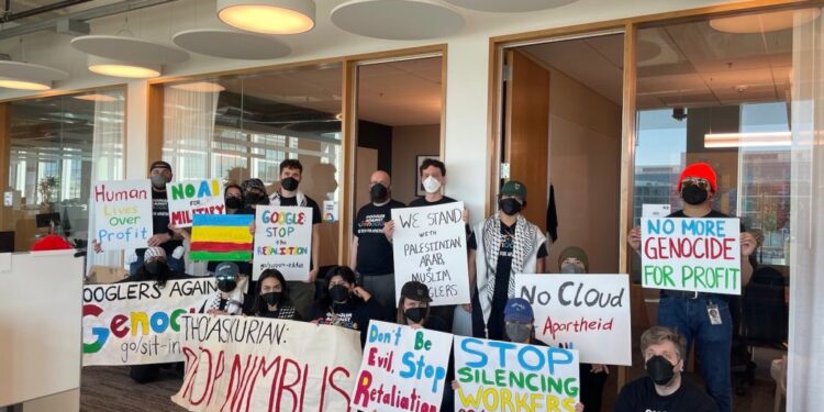 A large group of Google employees hold signs protesting their company's participation in "Project Nimbus."