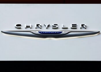 Chrysler logo on display at an auto show with a caption about recalling over 211,000 SUVs and pickup trucks due to a software malfunction