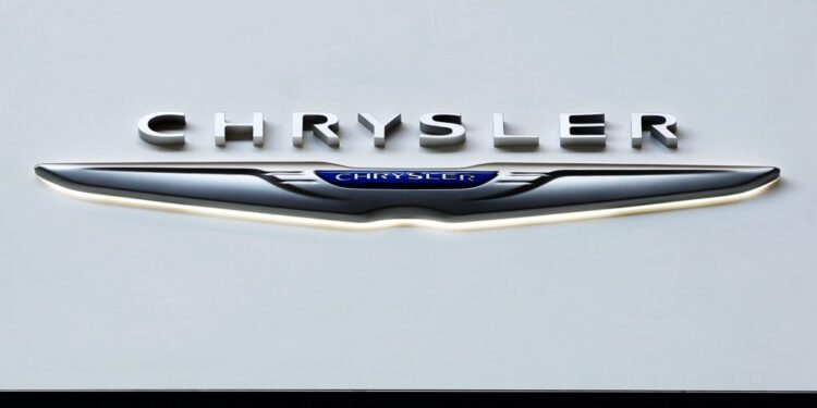 Chrysler logo on display at an auto show with a caption about recalling over 211,000 SUVs and pickup trucks due to a software malfunction