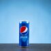 A can of Pepsi on a flat surface against a blue backdrop.