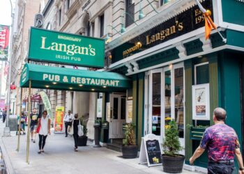 Group of people across the street from Langan's on 47th between 6th and 7th in New York, in front of a building under construction