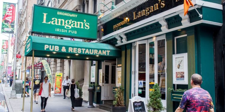 Group of people across the street from Langan's on 47th between 6th and 7th in New York, in front of a building under construction