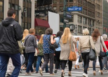 People commuting during rush hour across a busy Manhattan crosswalk in New York City.