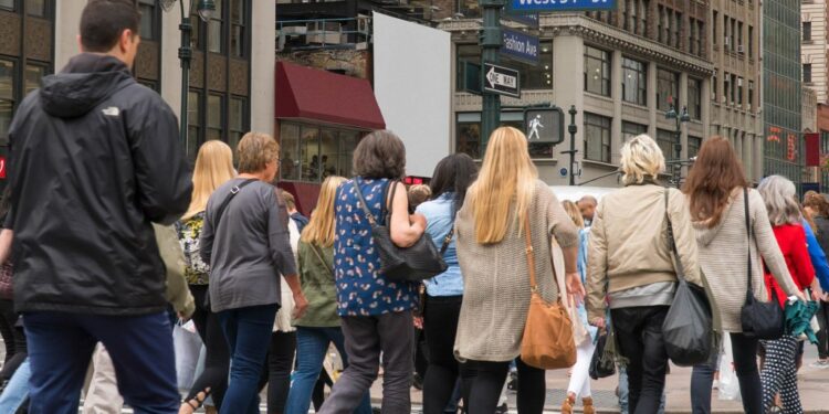 People commuting during rush hour across a busy Manhattan crosswalk in New York City.