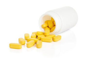 Yellow pills spilling out of a white bottle