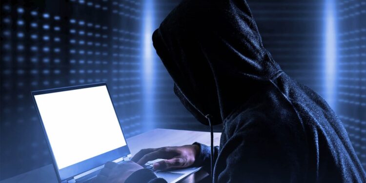 A person in a black hoodie using a laptop, symbolizing a data breach exposing personal information of individuals