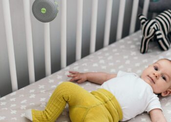 baby in crib with a small round noisemaker hanging on crib