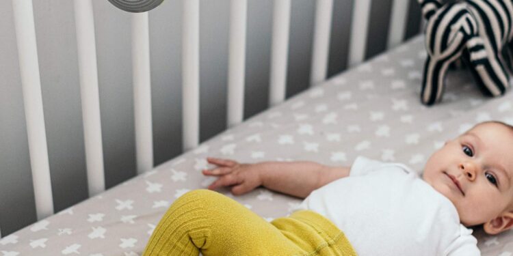 baby in crib with a small round noisemaker hanging on crib
