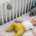baby in crib with a small round noisemaker hanging on crib