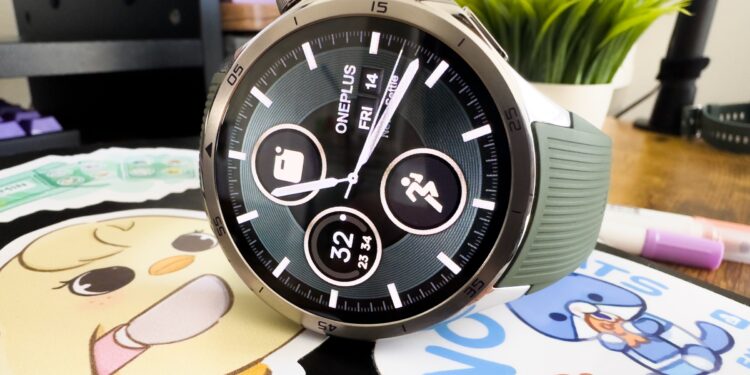 Close up of the OnePlus Watch 3 in emerald green. It sits on top of a black notebook with colorful cartoon stickers. You can also see a plant and pens in the background.