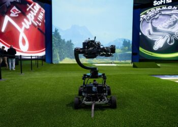 A photo of a camera, on wheels, in front of a large screen.