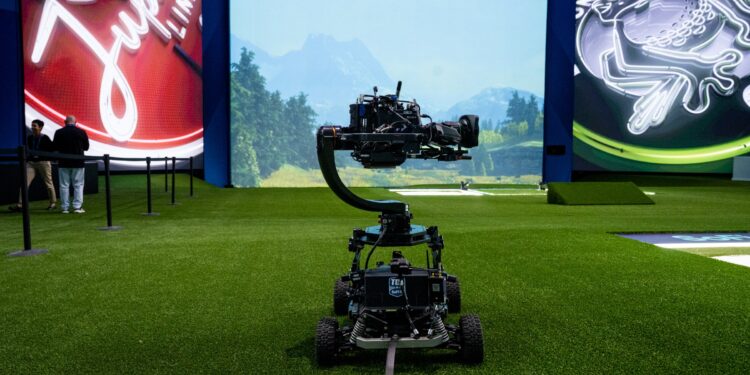 A photo of a camera, on wheels, in front of a large screen.