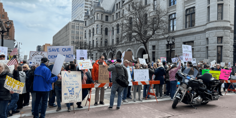 People holding protest signs while standing behind a barricade.