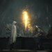 Screenshot from Elden Ring Nightreign featuring a shot of two characters, a person shrouded in white on the left and a person in armor sitting on the right in front of a glowing light.