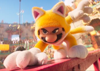 A man wearing a full body suit that makes him look like a fuzzy yellow cat and crouching on a steel beam in the middle of a colosseum.