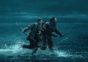 A man and a boy holding longbows while running on a path that’s being flooded by the rising tide.