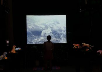 A dark room with a bright screen showing a digital jaguar. Several small jaguar statues surround a viewer in the center.