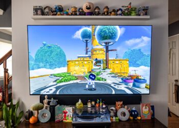 A TV set with a game on it, small figures lined up on a shelve above and a table top below.