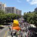 A parade balloon depicting Donald Trump as a baby wearing a diaper floats above a crowd of people marching down a street.