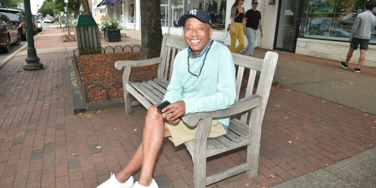 Russell Simmons sitting on a park bench, holding a phone.