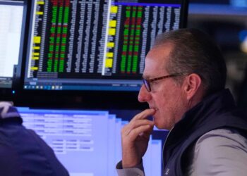 A stockbroker looks intently at computer screens displaying financial data.