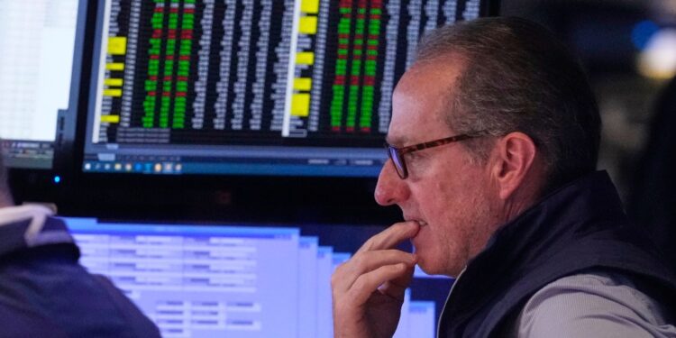 A stockbroker looks intently at computer screens displaying financial data.