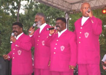 Four men in matching pink suits singing into microphones.