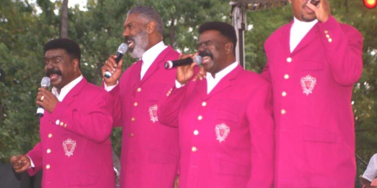 Four men in matching pink suits singing into microphones.