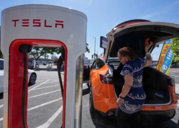 Woman charging an orange Tesla.