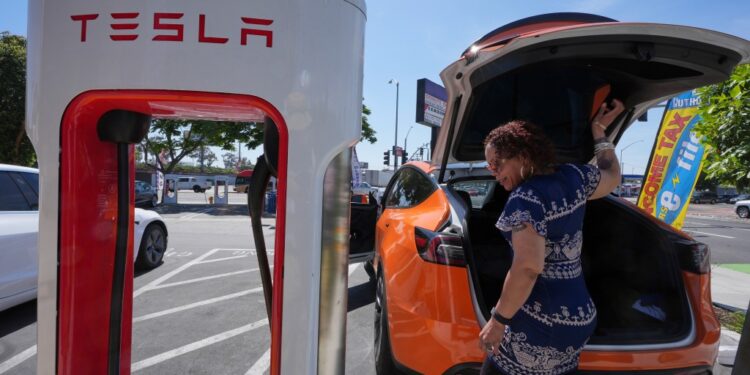 Woman charging an orange Tesla.