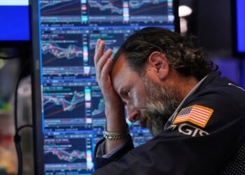 A stockbroker looking concerned at stock market data on multiple computer screens.