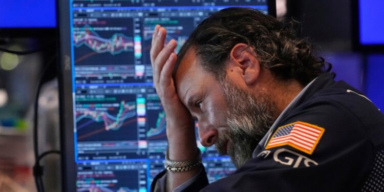 A stockbroker looking concerned at stock market data on multiple computer screens.