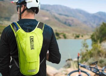 Biker rider wearing backpack with river and bike in background