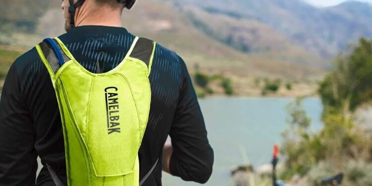 Biker rider wearing backpack with river and bike in background