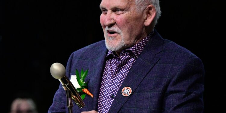Bernie Parent, former Philadelphia Flyers goalie, holds a microphone and trophy while speaking during a ceremony for Lou Nolan.